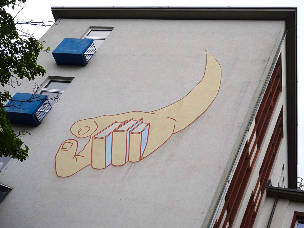 Hand mit Fingern aus Büchern an der Fassade der Schillerschule in Frankfurt