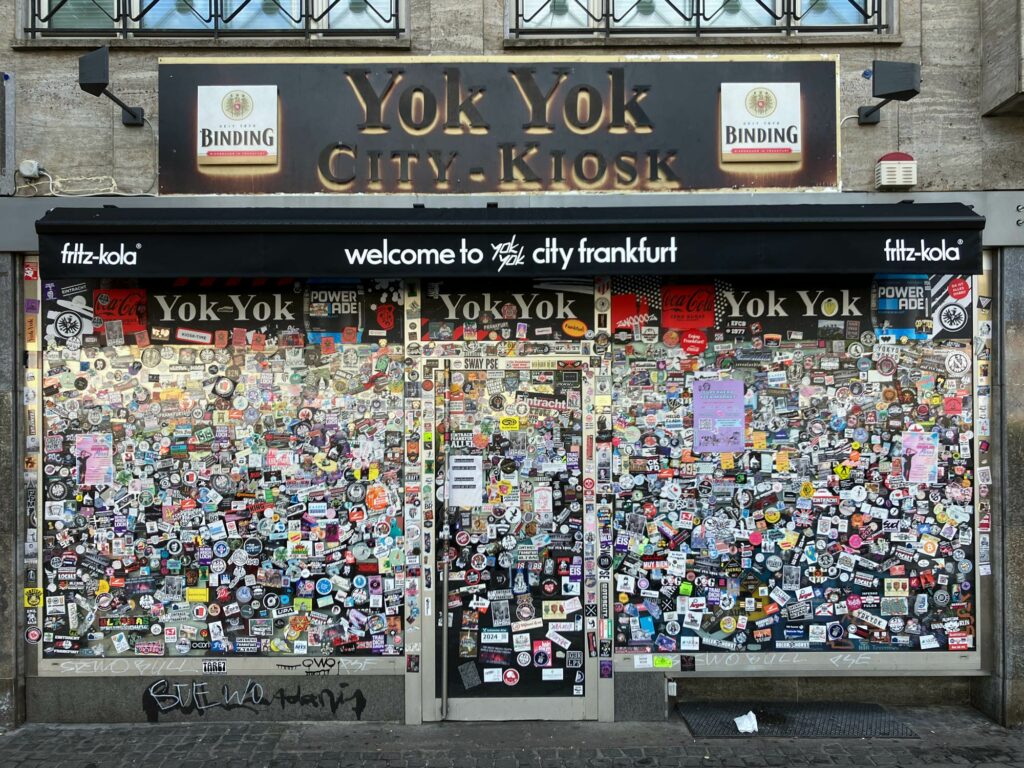 Schaufenster des Kiosks Yok Yok am neuen Standort mit Schaufenster voller Aufkleber
